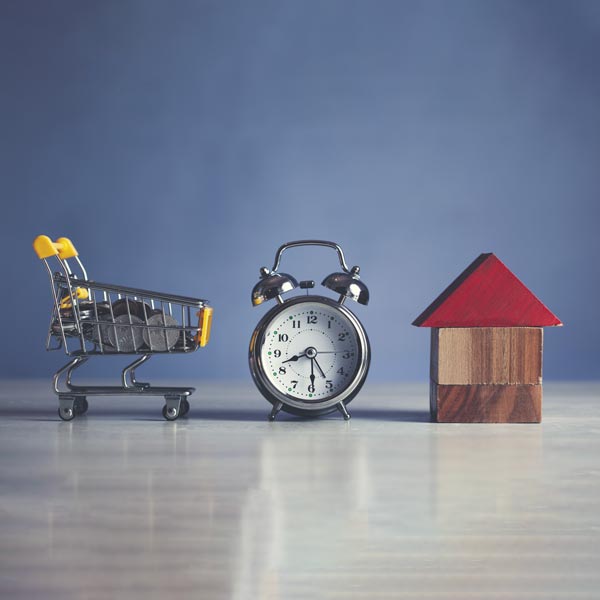 Vendita Immobiliare: carrello spessa del supermercato, orologio e una casa miniatura su un tavolo